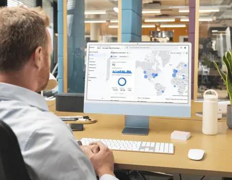 Persoon aan bureau bekijkt Google Analytics-dashboard met grafieken en kaarten over websiteverkeer.