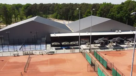 Tennis complex with clay courts and a modern building, surrounded by trees.